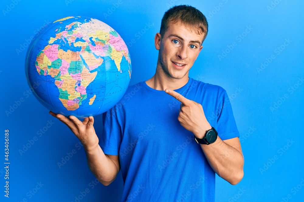 Young caucasian man holding world ball smiling happy pointing with hand and finger Young caucasian man holding world ball smiling happy pointing with hand and finger