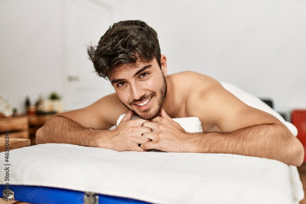 Young hispanic man smiling happy lying on the table at beauty center. Young hispanic man smiling happy lying on the table at beauty center.