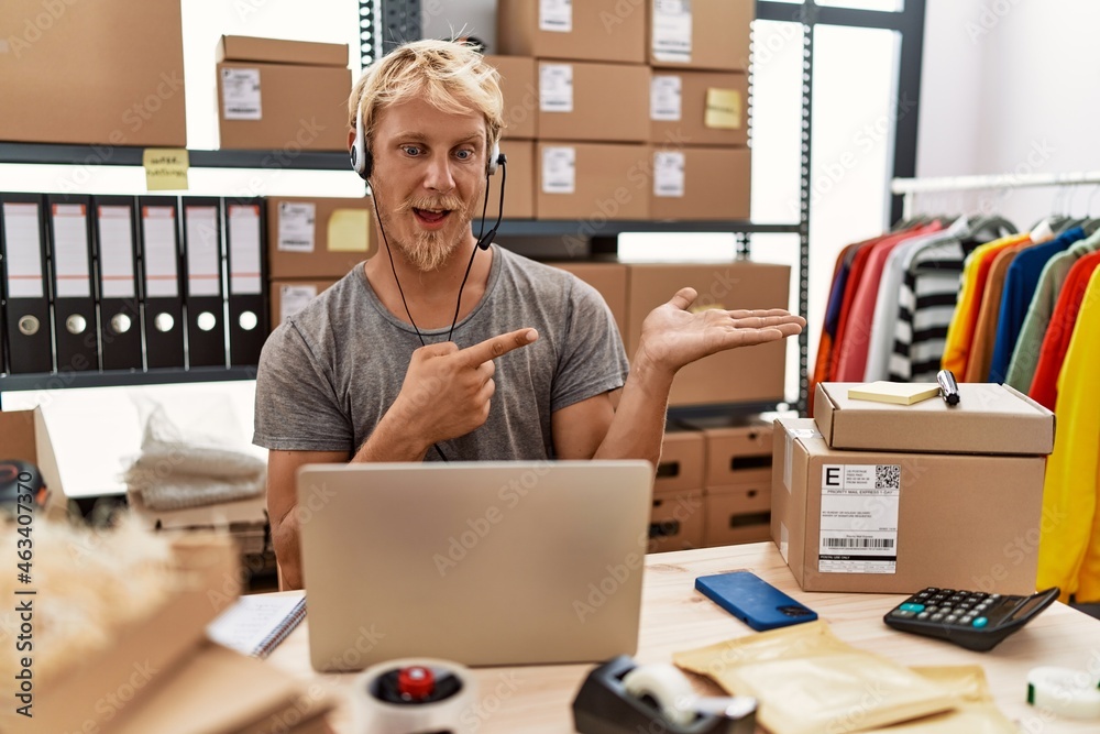 Young blond man wearing operator headset working at online shop amazed and smiling to the camera while presenting with hand and pointing with finger. Young blond man wearing operator headset working at online shop amazed and smiling to the camera while presenting with hand and pointing with finger.