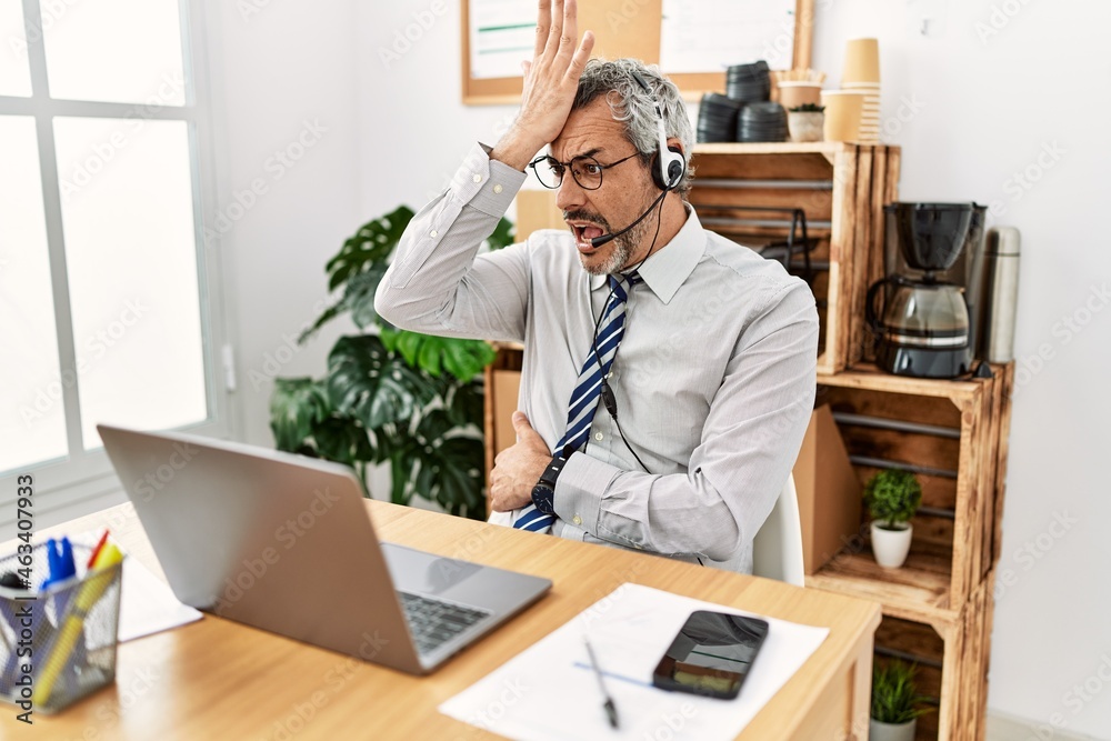 Middle age hispanic business man working at the office wearing operator headset surprised with hand on head for mistake, remember error. forgot, bad memory concept. Middle age hispanic business man working at the office wearing operator headset surprised with hand on head for mistake, remember error. forgot, bad memory concept.