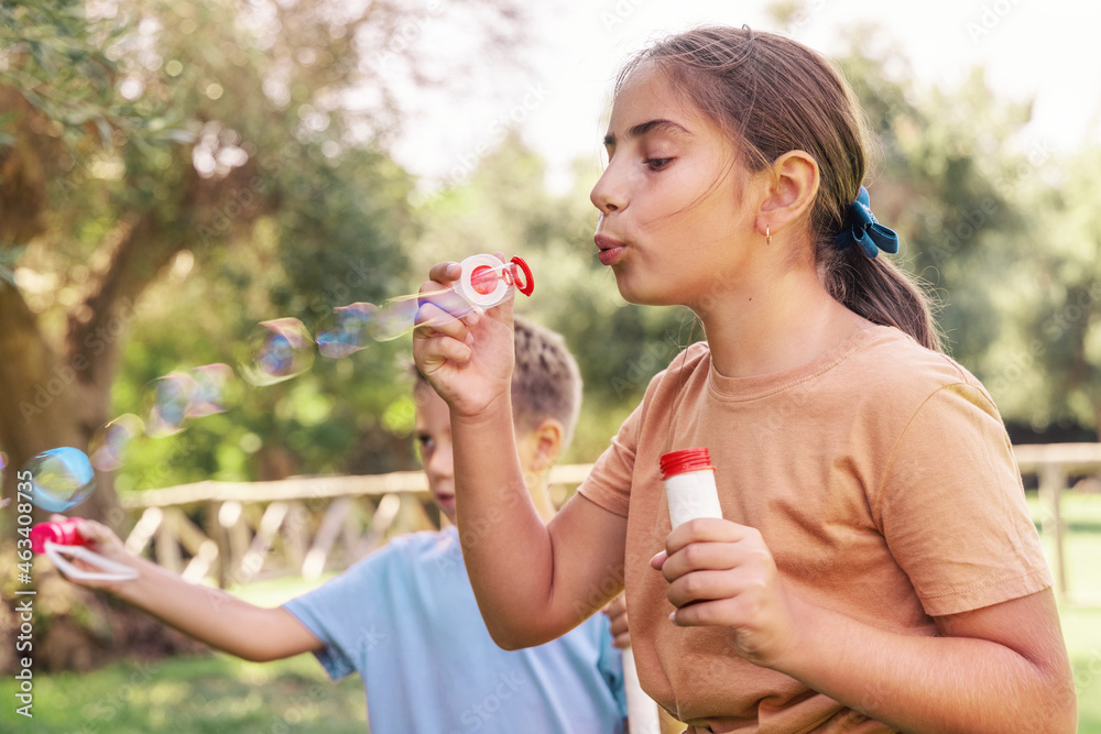 Kid girl and boy blowing soap bubbles in a park