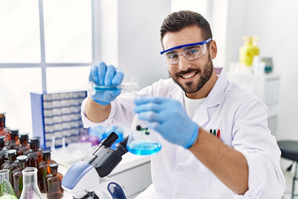 Young hispanic man wearing scientist uniform mixing liquid at laboratory Young hispanic man wearing scientist uniform mixing liquid at laboratory