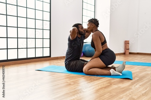 Young african american sporty couple kissing and doing abs exercise at sport center.