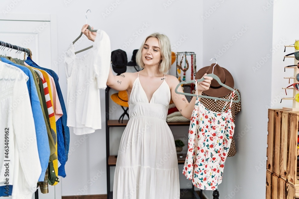 Young caucasian woman smiling confident holding clothes at clothing store
