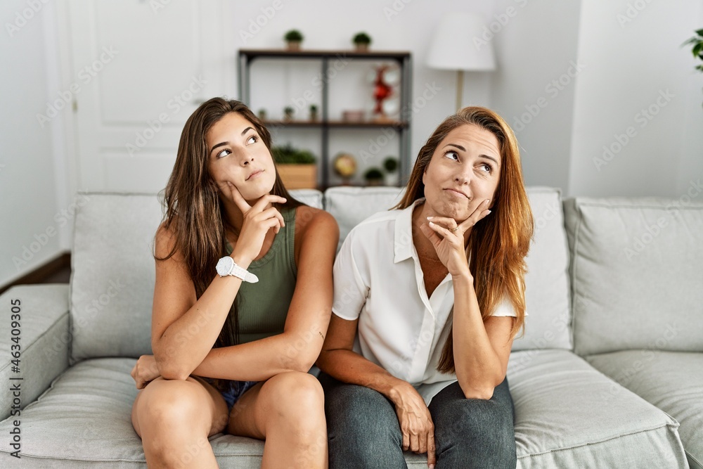 Mother and daughter together sitting on the sofa at home with hand on chin thinking about question, pensive expression. smiling with thoughtful face. doubt concept. Mother and daughter together sitting on the sofa at home with hand on chin thinking about question, pensive expression. smiling with thoughtful face. doubt concept.