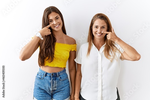 Mother and daughter together standing together over isolated background pointing with hand finger to face and nose, smiling cheerful. beauty concept