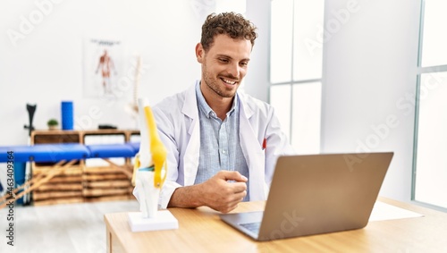 Young hispanic man wearing physiotherapist uniform having video call working at clinic