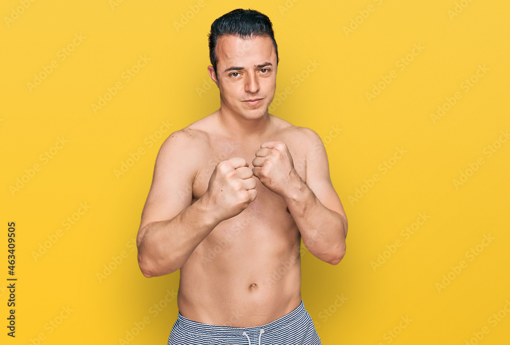 Handsome young man wearing swimwear shirtless ready to fight with fist defense gesture, angry and upset face, afraid of problem