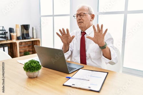 Photography Senior man working at the office using computer laptop moving away hands palms showing refusal and denial with afraid and disgusting expression