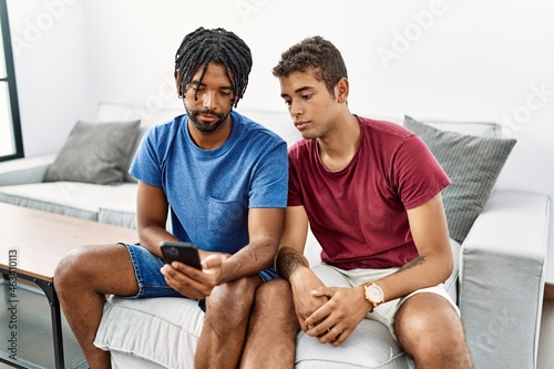 Young hispanic men using smartphone sitting on the sofa at home relaxed with serious expression on face. simple and natural looking at the camera.