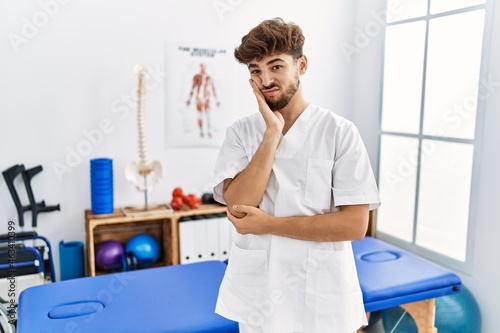 Young arab man working at pain recovery clinic thinking looking tired and bored with depression problems with crossed arms.