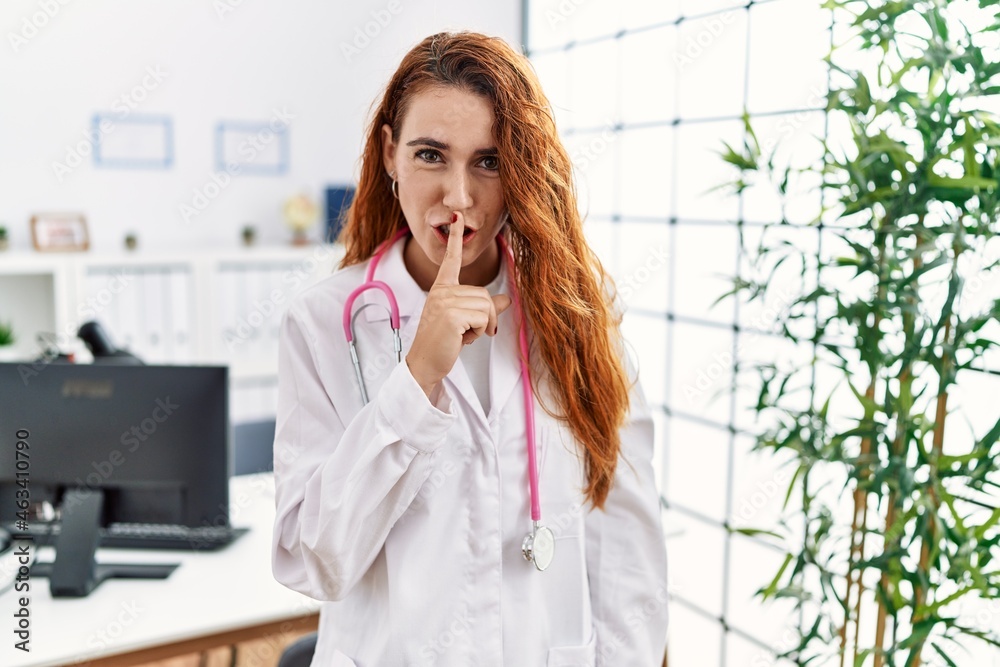 Young redhead woman wearing doctor uniform and stethoscope at the clinic asking to be quiet with finger on lips. silence and secret concept. Young redhead woman wearing doctor uniform and stethoscope at the clinic asking to be quiet with finger on lips. silence and secret concept.