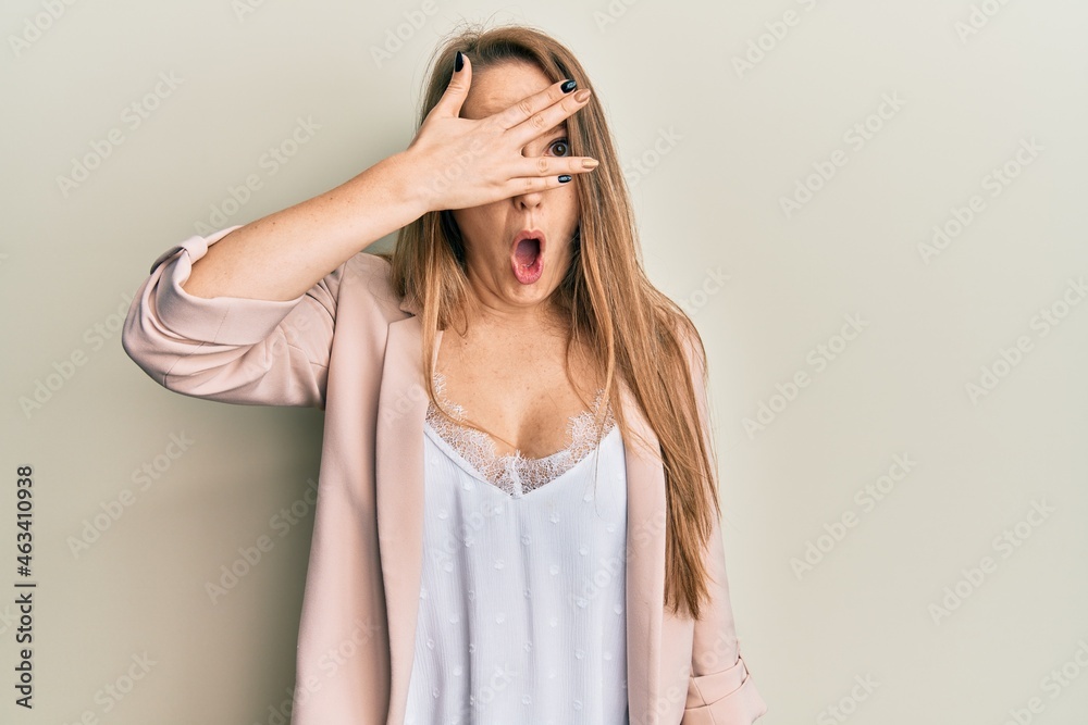 Young blonde woman wearing business jacket and glasses peeking in shock covering face and eyes with hand, looking through fingers with embarrassed expression. Young blonde woman wearing business jacket and glasses peeking in shock covering face and eyes with hand, looking through fingers with embarrassed expression.