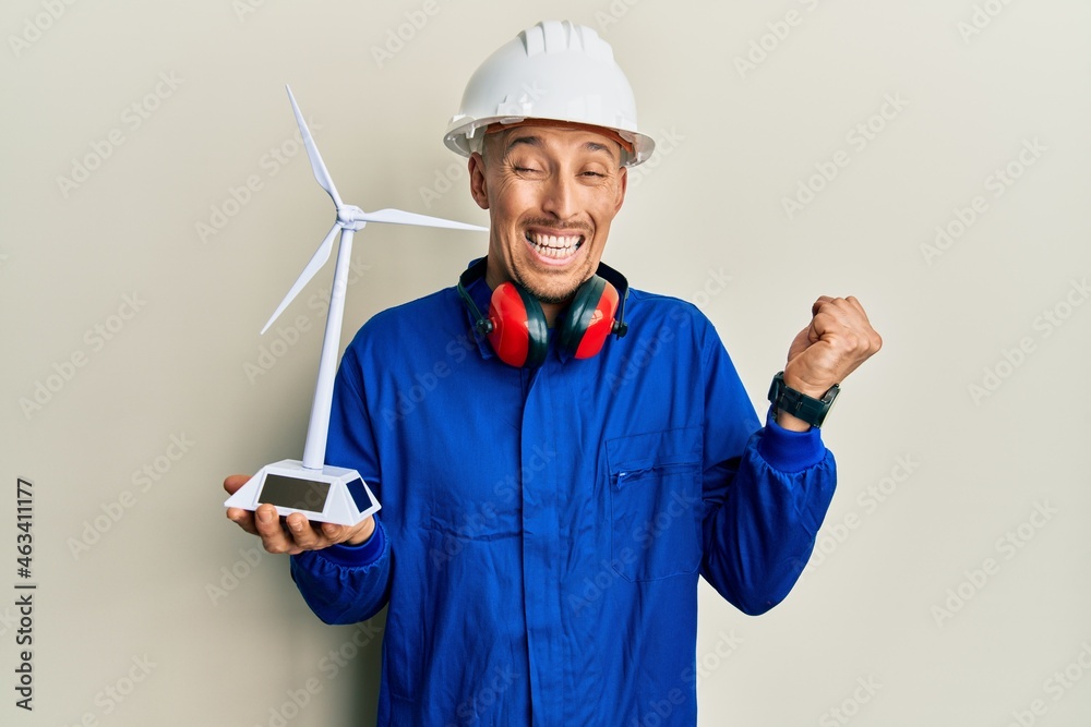 Bald engineer man with beard holding solar windmill for renewable electricity screaming proud, celebrating victory and success very excited with raised arm