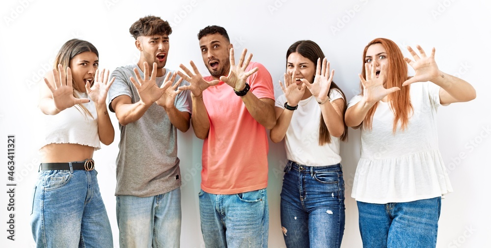 Obraz premium Group of young friends standing together over isolated background afraid and terrified with fear expression stop gesture with hands, shouting in shock. panic concept.