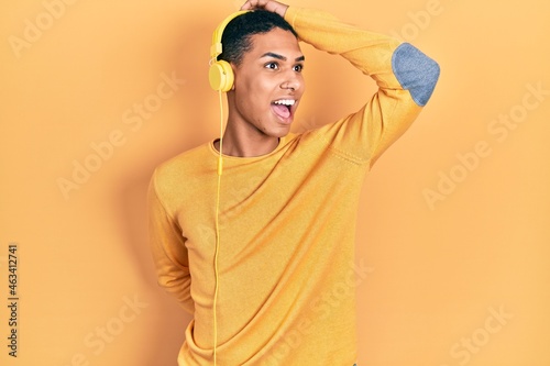 Young african american guy listening to music using headphones smiling confident touching hair with hand up gesture, posing attractive and fashionable