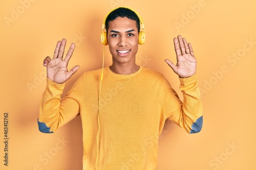 Young african american guy listening to music using headphones showing and pointing up with fingers number nine while smiling confident and happy. © Krakenimages.com