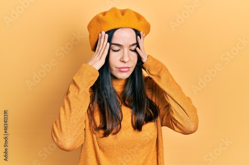 Young brunette woman wearing french look with beret with hand on head, headache because stress. suffering migraine.