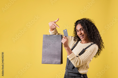mujer afroamericana en fondo amarillo de estudio señalando una tarjeta plástica de compras de crédito o debito 