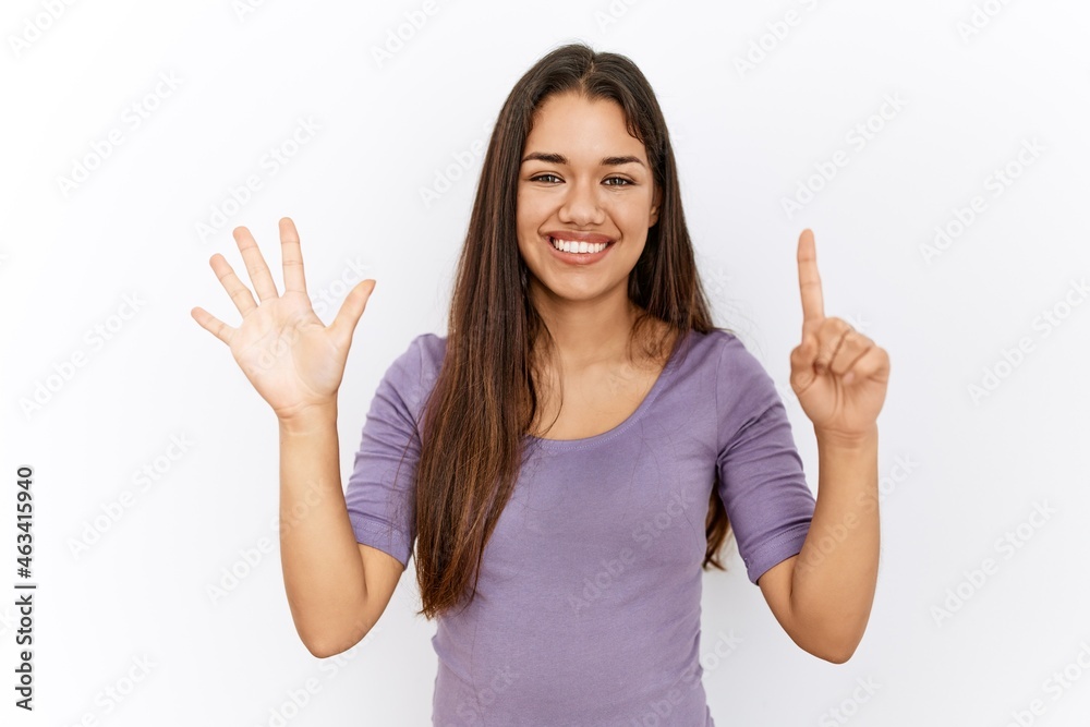 Young brunette woman standing by isolated background showing and pointing up with fingers number six while smiling confident and happy. Young brunette woman standing by isolated background showing and pointing up with fingers number six while smiling confident and happy.