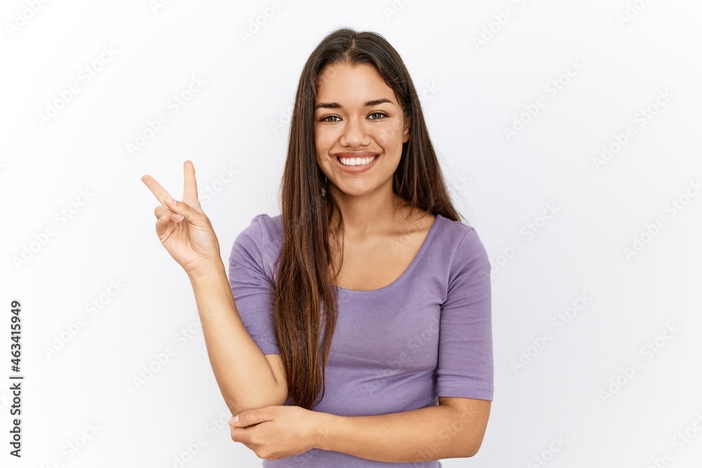 Young brunette woman standing by isolated background smiling with happy face winking at the camera doing victory sign. number two. Young brunette woman standing by isolated background smiling with happy face winking at the camera doing victory sign. number two.