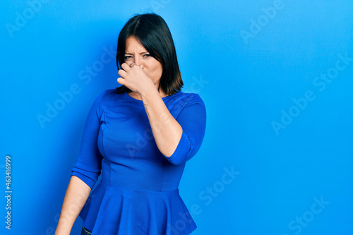 Young hispanic woman wearing casual clothes smelling something stinky and disgusting, intolerable smell, holding breath with fingers on nose. bad smell