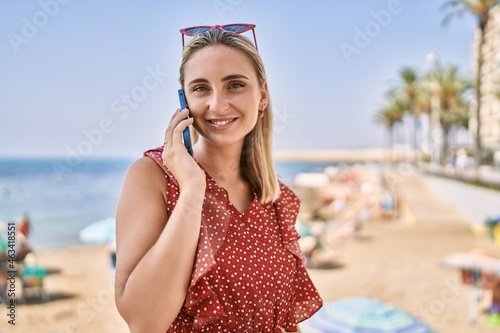 Young blonde girl smiling happy talking on the smartphone at the beach