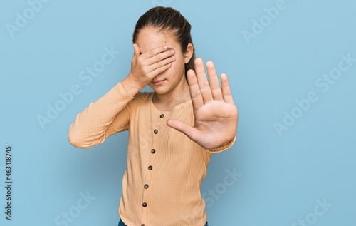 Beautiful brunette little girl wearing casual sweater covering eyes with hands and doing stop gesture with sad and fear expression. embarrassed and negative concept. photo