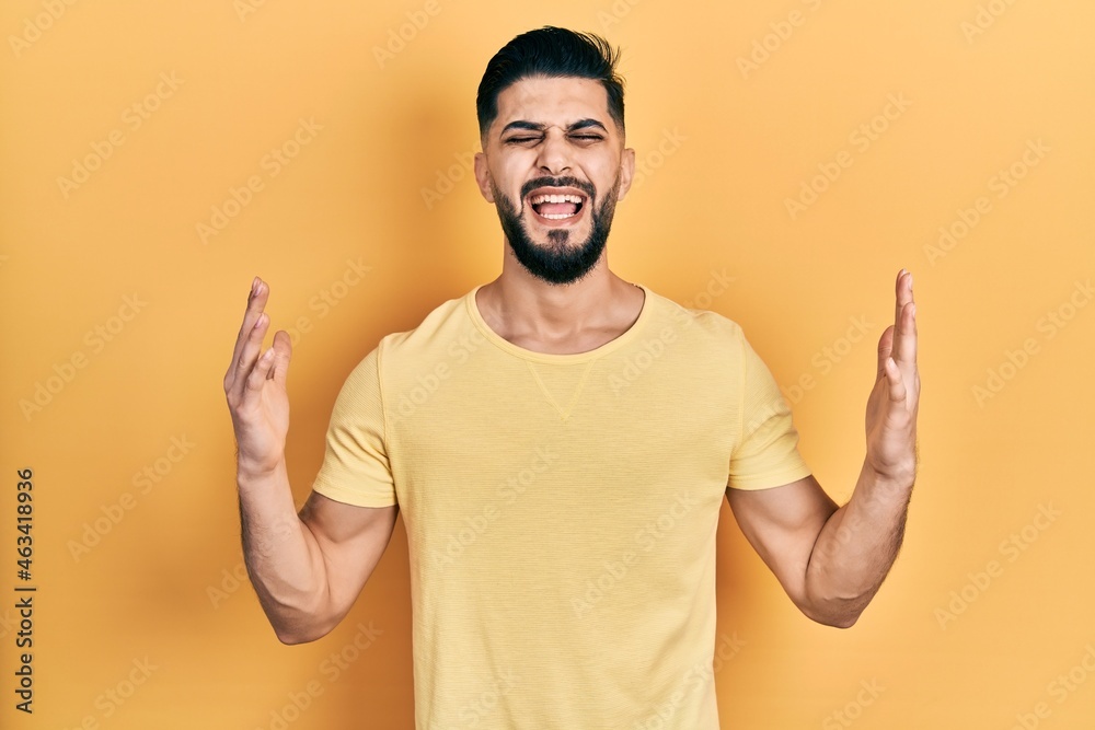 Handsome man with beard wearing casual yellow t shirt celebrating mad and crazy for success with arms raised and closed eyes screaming excited. winner concept Handsome man with beard wearing casual yellow t shirt celebrating mad and crazy for success with arms raised and closed eyes screaming excited. winner concept
