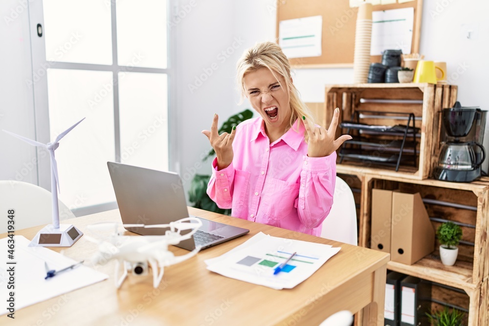 Young caucasian woman working at the office shouting with crazy expression doing rock symbol with hands up. music star. heavy concept. Young caucasian woman working at the office shouting with crazy expression doing rock symbol with hands up. music star. heavy concept.
