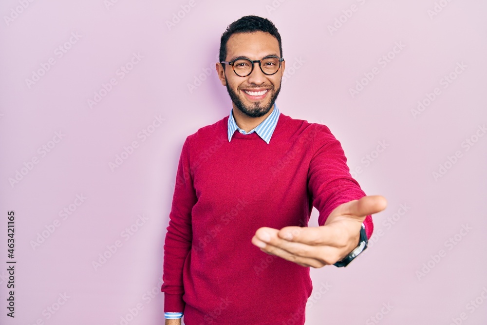 Hispanic man with beard wearing business shirt and glasses smiling cheerful offering palm hand giving assistance and acceptance. Hispanic man with beard wearing business shirt and glasses smiling cheerful offering palm hand giving assistance and acceptance.