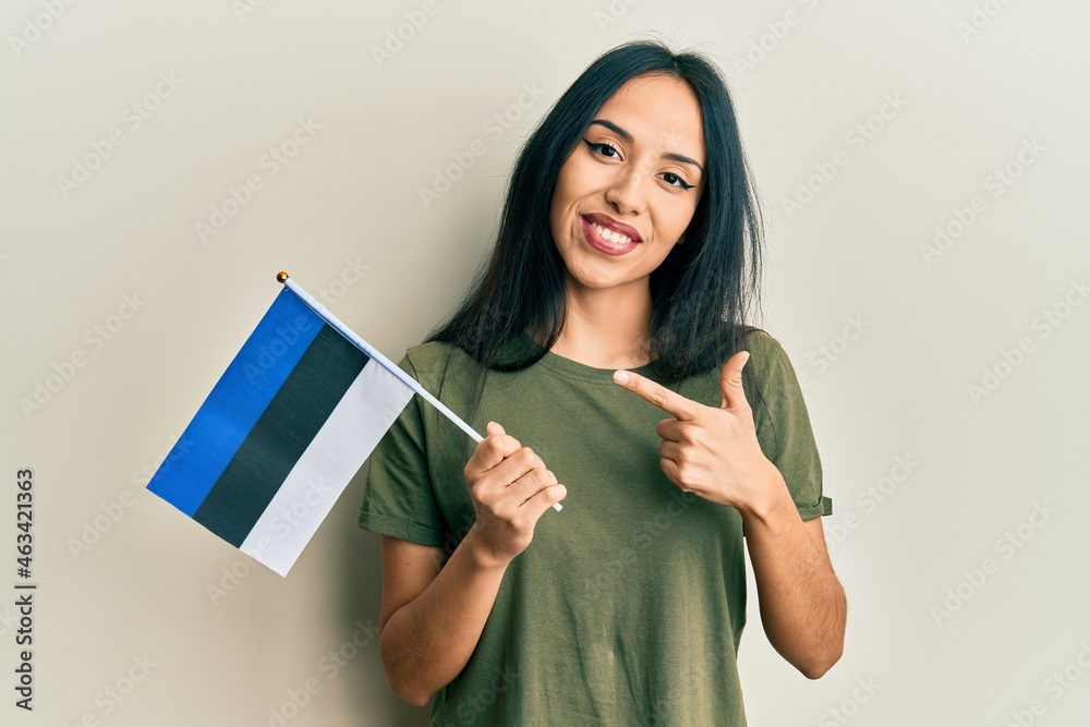 Fototapeta premium Young hispanic girl holding estonia flag smiling happy pointing with hand and finger