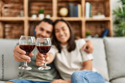 Young latin couple smiling happy toasting with red wine glass at home.