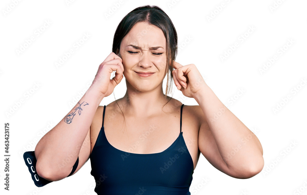 Young hispanic woman wearing sportswear covering ears with fingers with annoyed expression for the noise of loud music. deaf concept. Young hispanic woman wearing sportswear covering ears with fingers with annoyed expression for the noise of loud music. deaf concept.