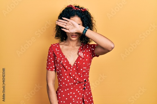 Young latin girl wearing summer dress covering eyes with arm  looking serious and sad. sightless  hiding and rejection concept