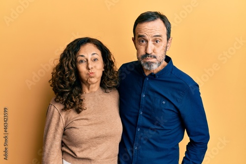 Middle age hispanic couple wearing casual clothes puffing cheeks with funny face. mouth inflated with air  crazy expression.