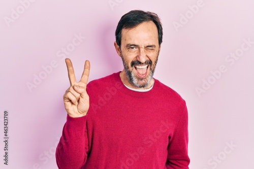 Middle age hispanic man wearing casual clothes smiling with happy face winking at the camera doing victory sign. number two.