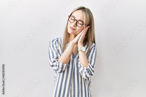 Asian young woman wearing casual clothes and glasses sleeping tired dreaming and posing with hands together while smiling with closed eyes.