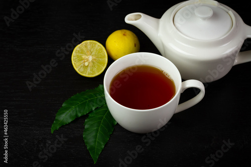 Neem tea in ceramic cup with neem leaf and lemon on black wooden background dark tone.
