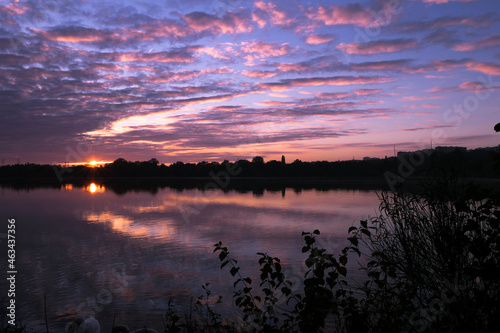 Purple and pink landscape of sunrise or sunset over a lake. Reflection of the clouds in the water. Symmetry of a dramatic sky.