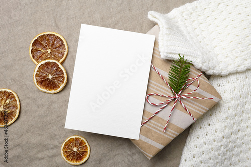 Christmas greeting card mockup with decorated gift box, knitted sweater and dry oranges
