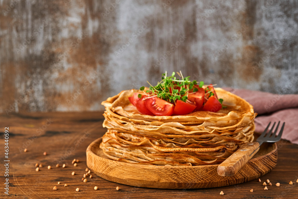 Stack of gluten free buckwheat flour crepes pancakes with cherry tomatoes and arugula microgreens on wooden plate, homemade healthy baking for breakfast. Stack of gluten free buckwheat flour crepes pancakes with cherry tomatoes and arugula microgreens on wooden plate, homemade healthy baking for breakfast.