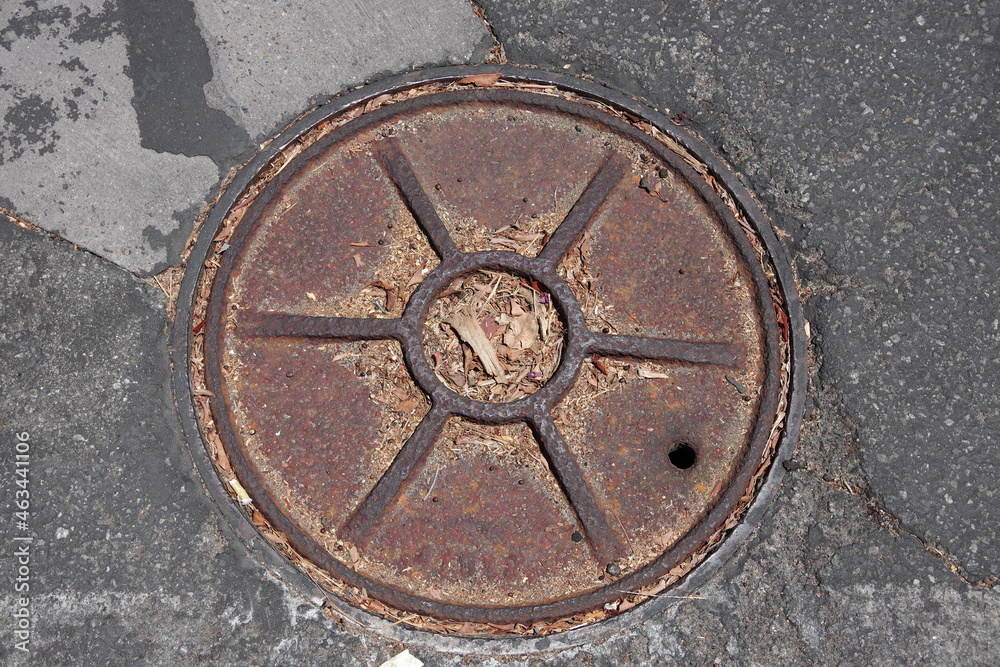 Close-up view of an iron cover plate for a sewer line in the asphalt of a street