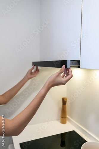 woman select mode on cooking hood, standing near kitchen appliance in modern interior house.