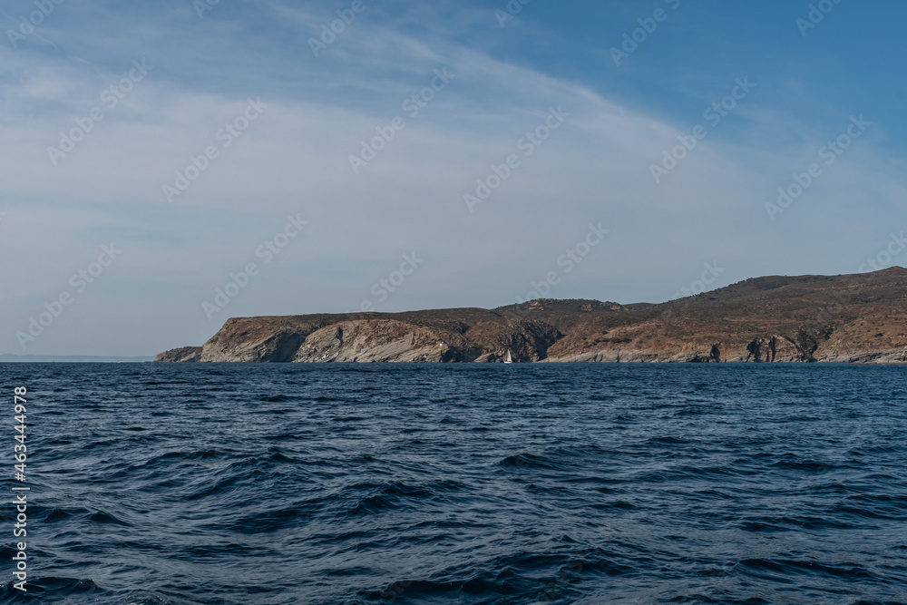 Seaside cliffs and sailboat with Calanans lighthouse next to Cadaques and S'Ocelleta headland, Catalonia, Spain.