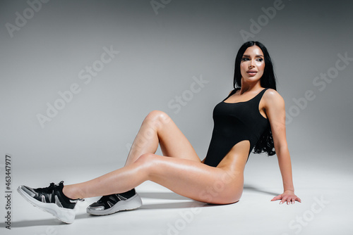 Young sexy brunette in a black bodysuit on a white background. The perfect athletic figure.
