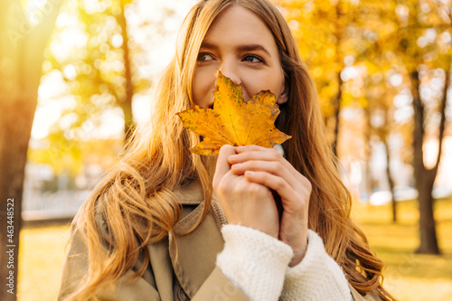 beautiful woman in a beige raincoat shows a yellow leaf that has fallen from a tree. autumn weather
