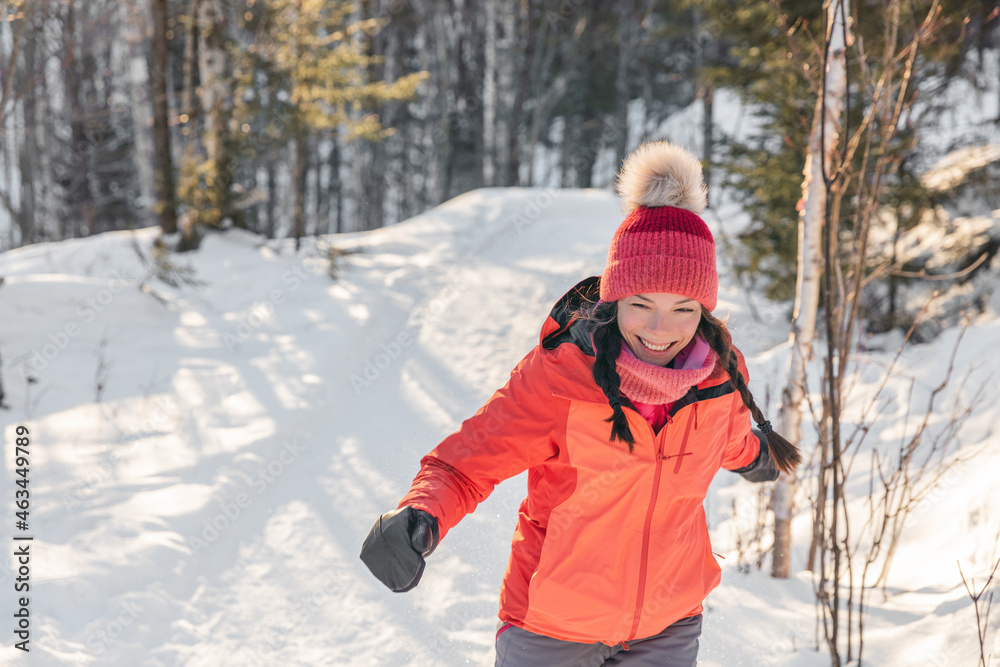 Happy Asian woman laughing walking in snow forest during winter. Beautiful portrait of young adult smiling wearing cold weather hat and gloves, orange jacket