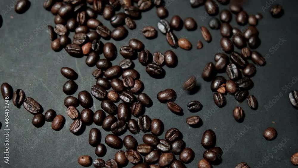 Bunch of roasted coffee beans being poured onto black surface Bunch of roasted coffee beans being poured onto black surface