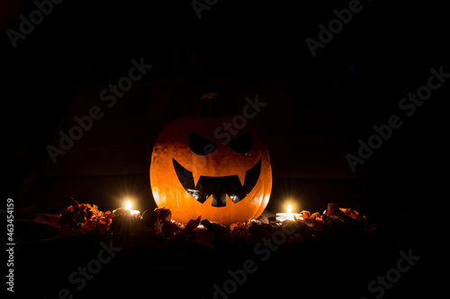 Halloween Background Of A Pumpkin Surrounded By Dry Leaves And With Candles, On A Black Background.